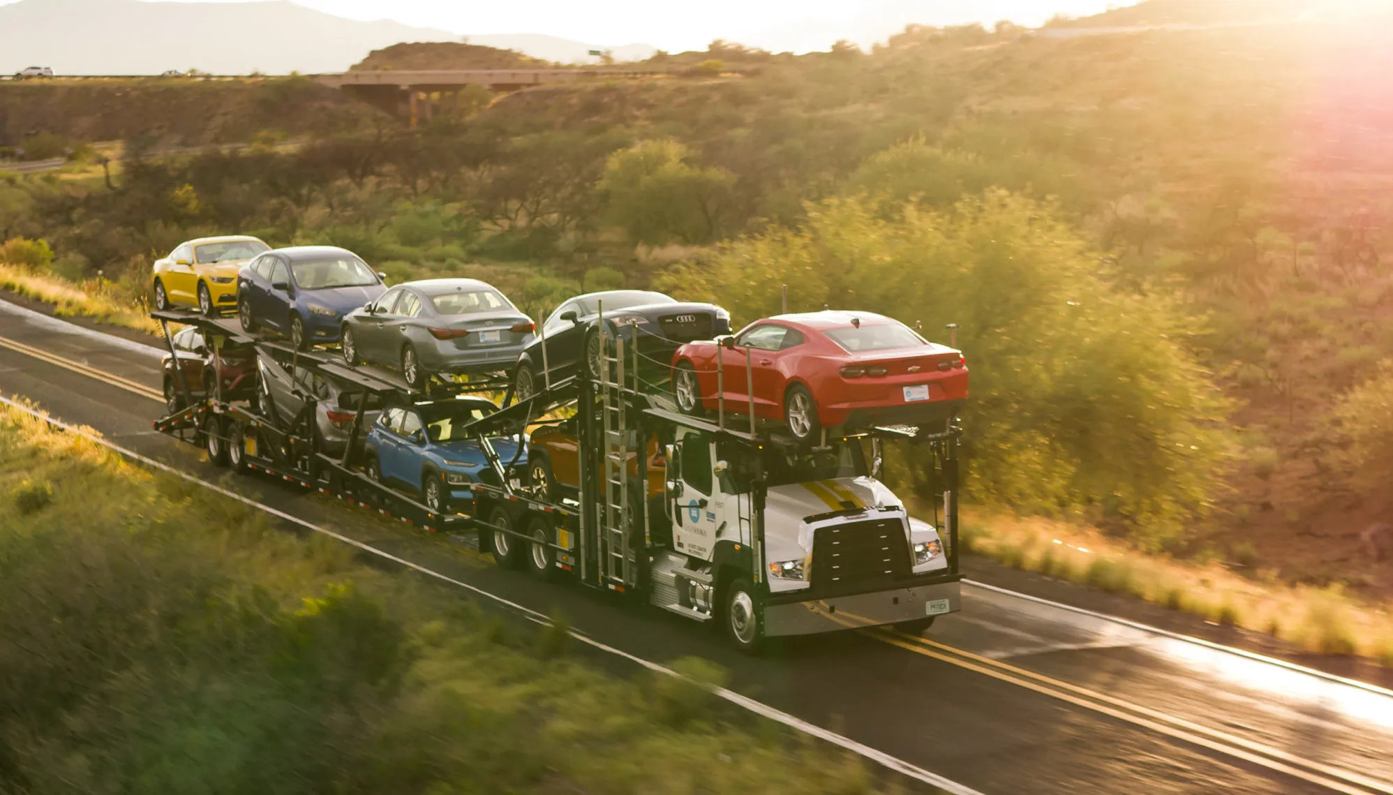 Auto transport truck carrying cars on a highway at sunset
